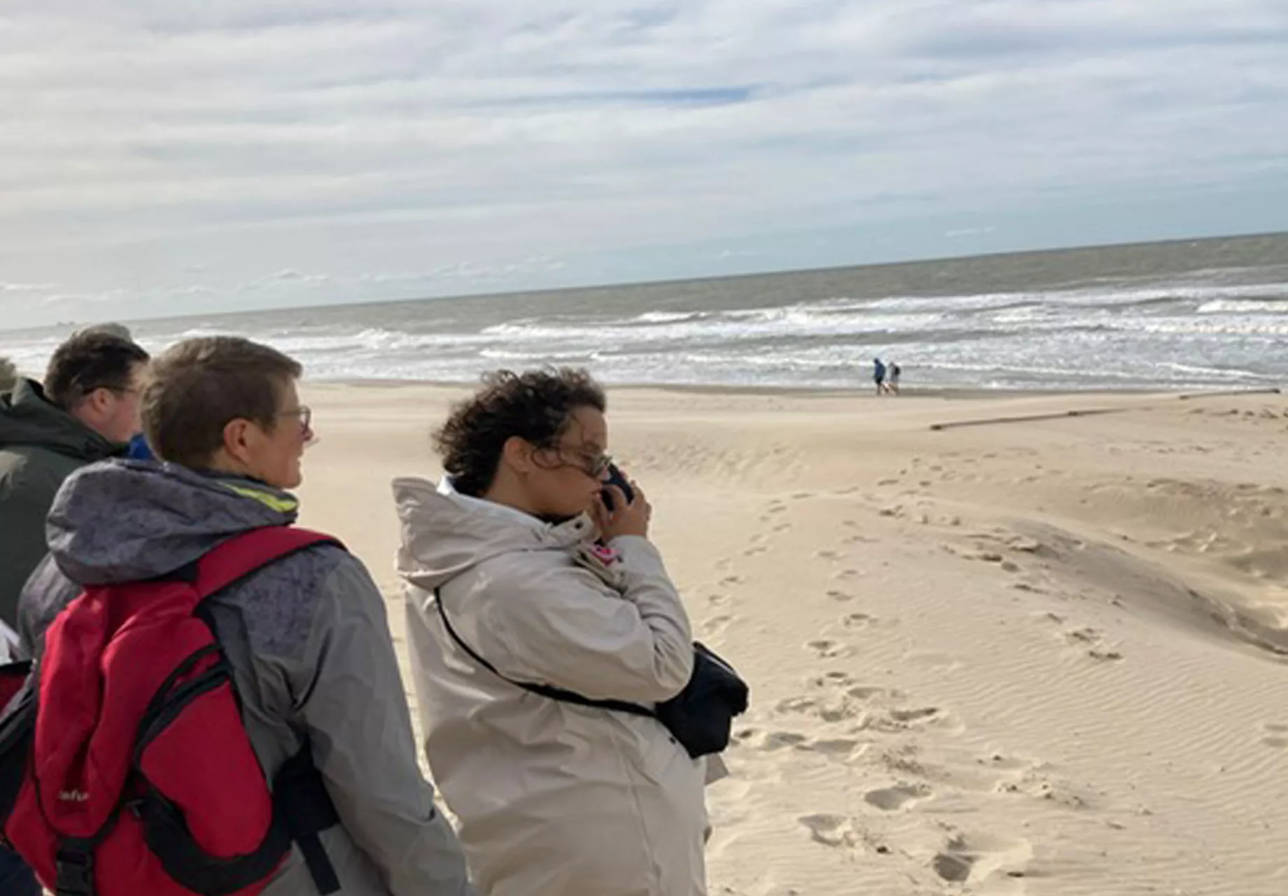 3 personen staan op het strand met hun gezicht naar de zee