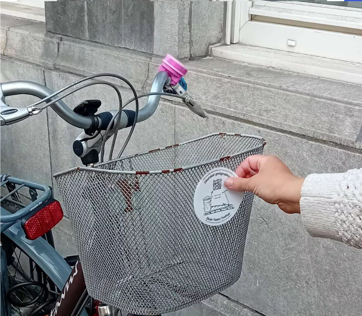  Iemand kleeft een Team Trottoir-sticker op het mandje van een slecht geparkeerde fiets. Op de foto staat de tekst: Woensdag 21/10, Antwerpen. 